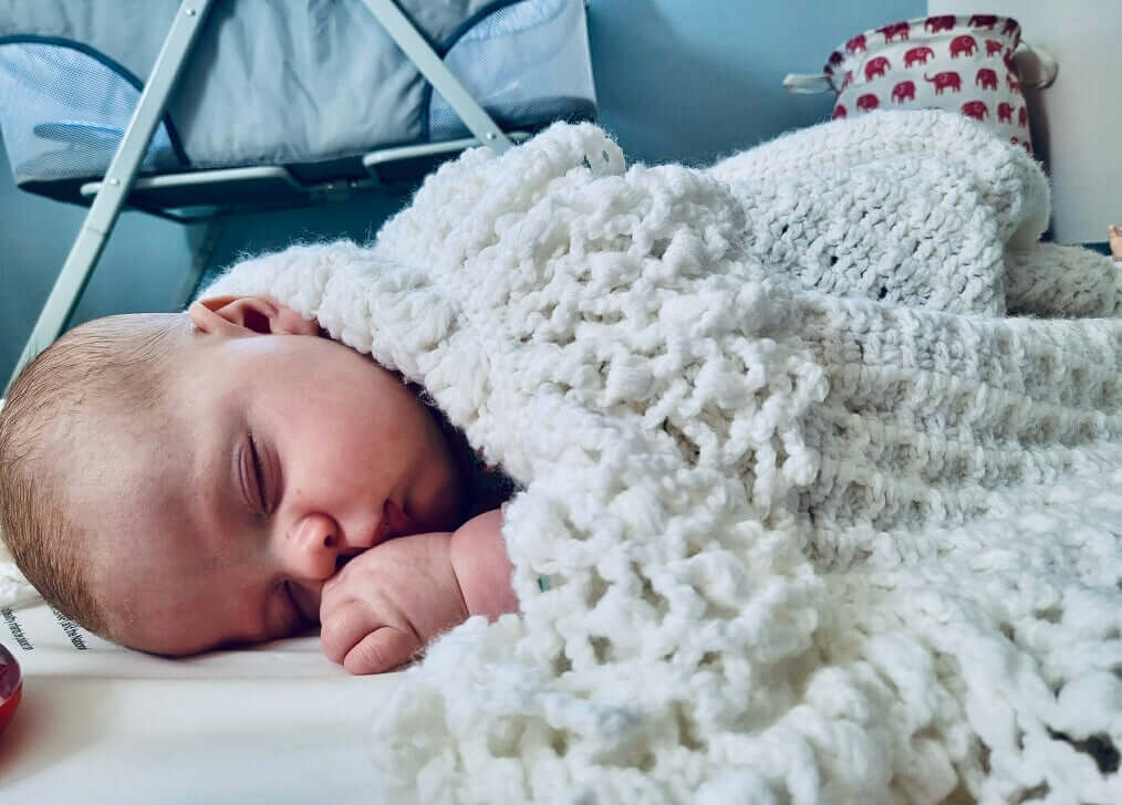 A sleeping baby wrapped in a soft white blanket, resting peacefully in a cozy room.