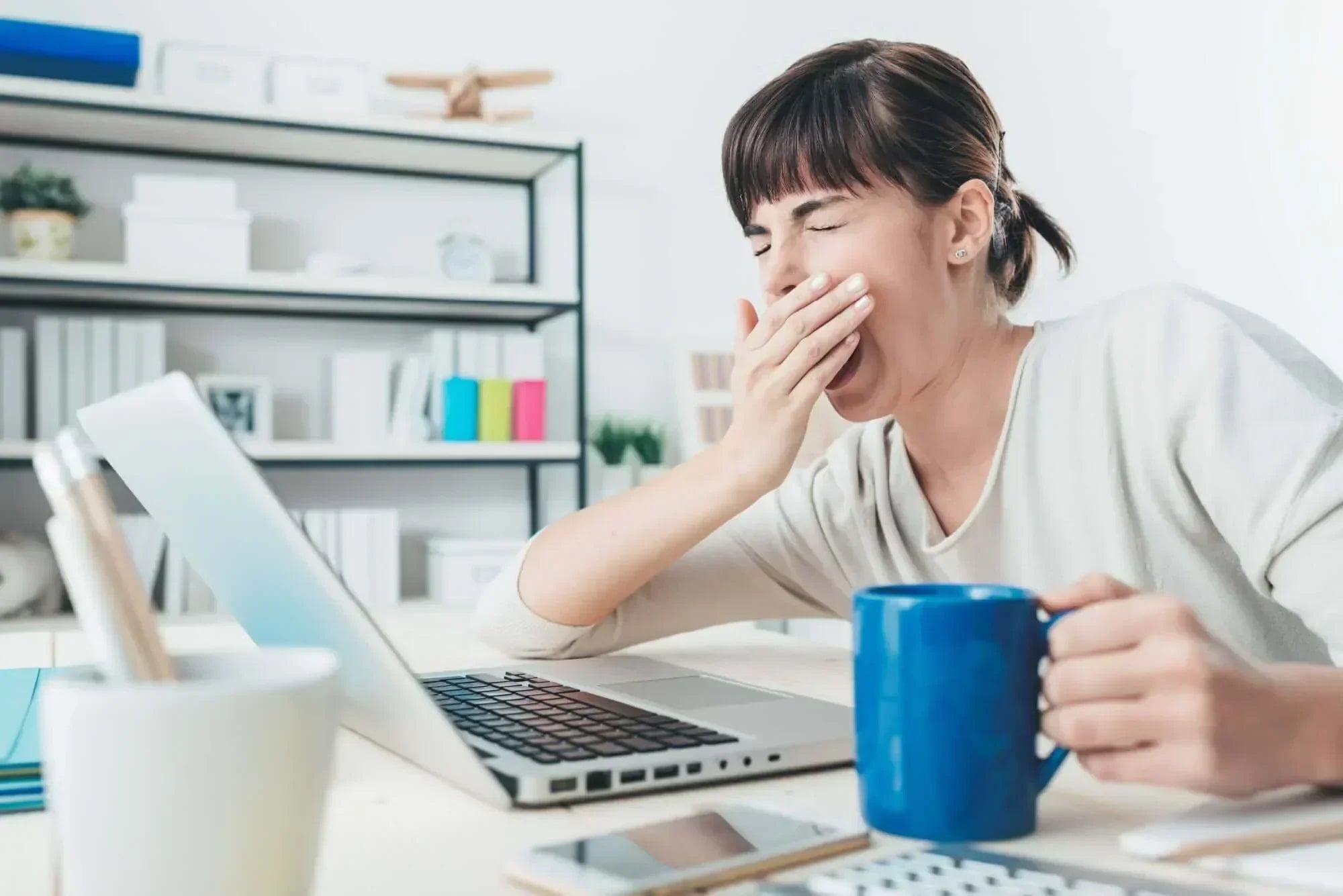 Woman yawning while using a laptop, illustrating the need for sleep quality improvement strategies.