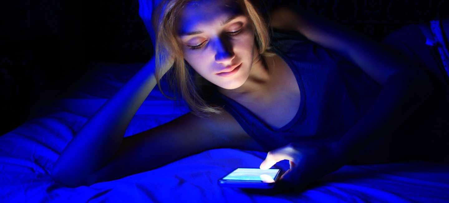 Young person in bed using a smartphone in blue light, highlighting blue light sleep disruption.