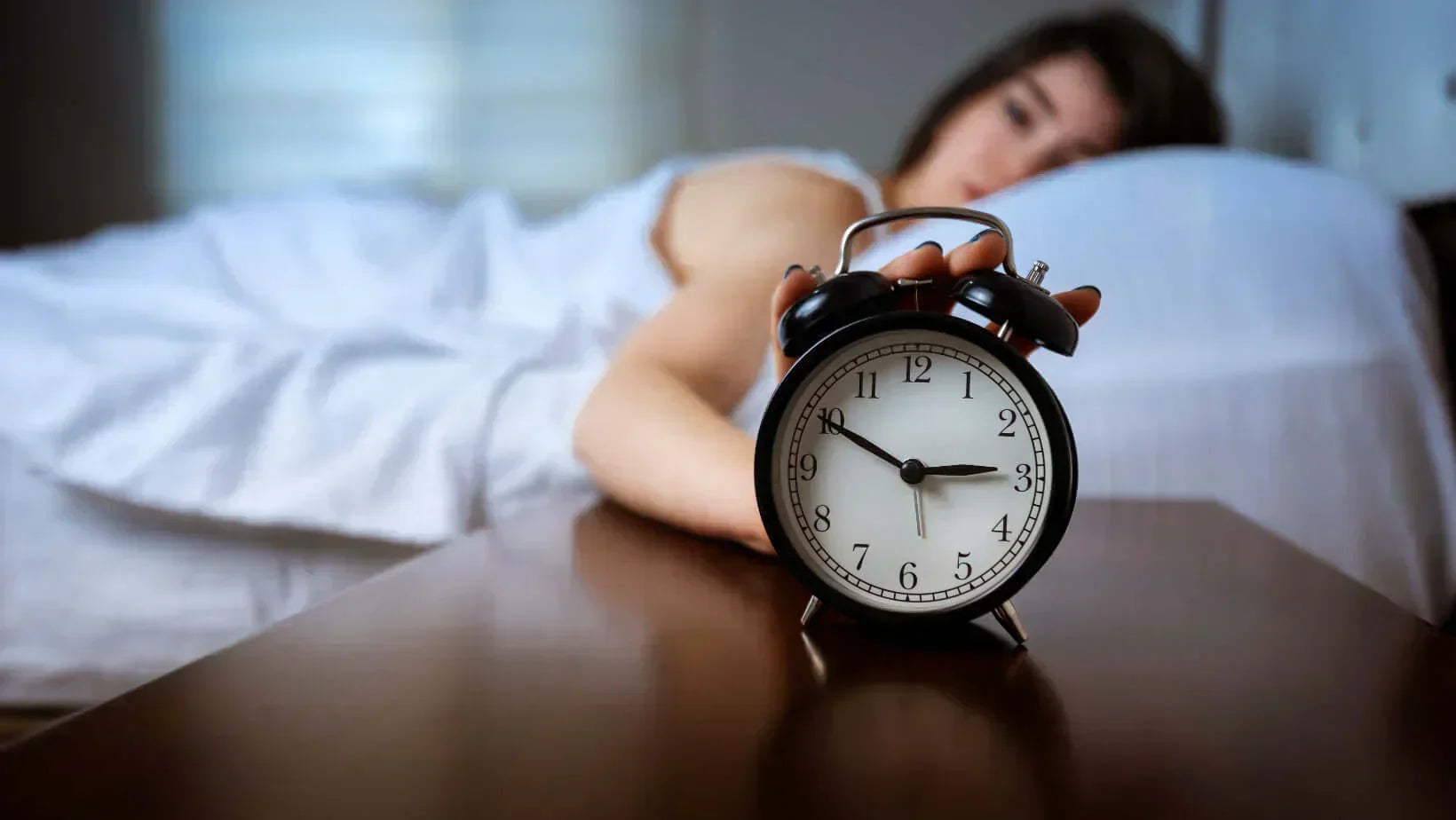 A person struggling with sleep beside an alarm clock, highlighting natural insomnia remedies.