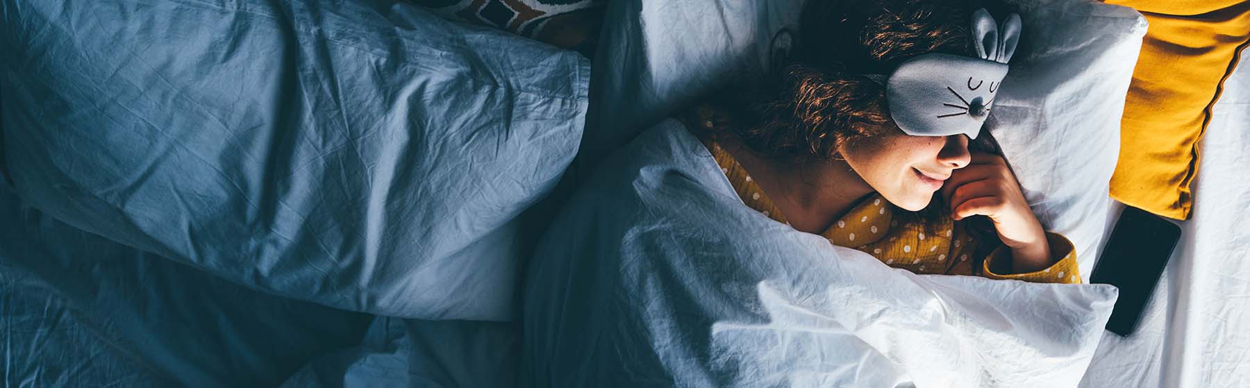 A person sleeping peacefully under a blanket, wearing a sleep mask, illustrating anxiety and sleep.