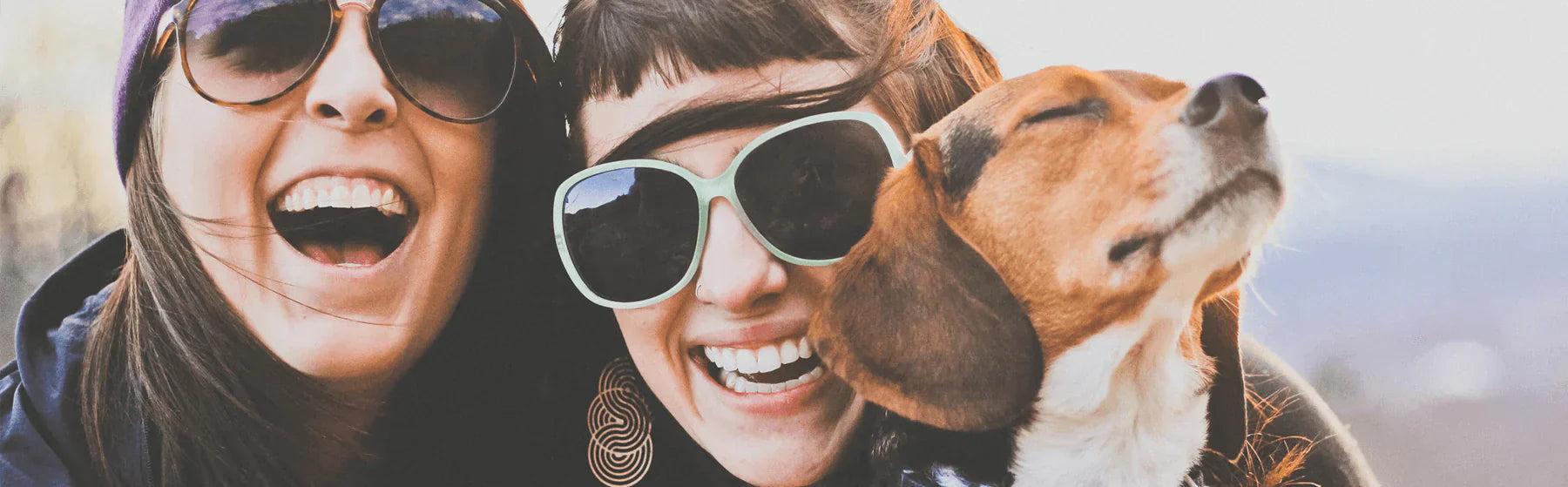 Two women laughing joyfully with a dog, showcasing holistic wellness benefits through happiness and connection.