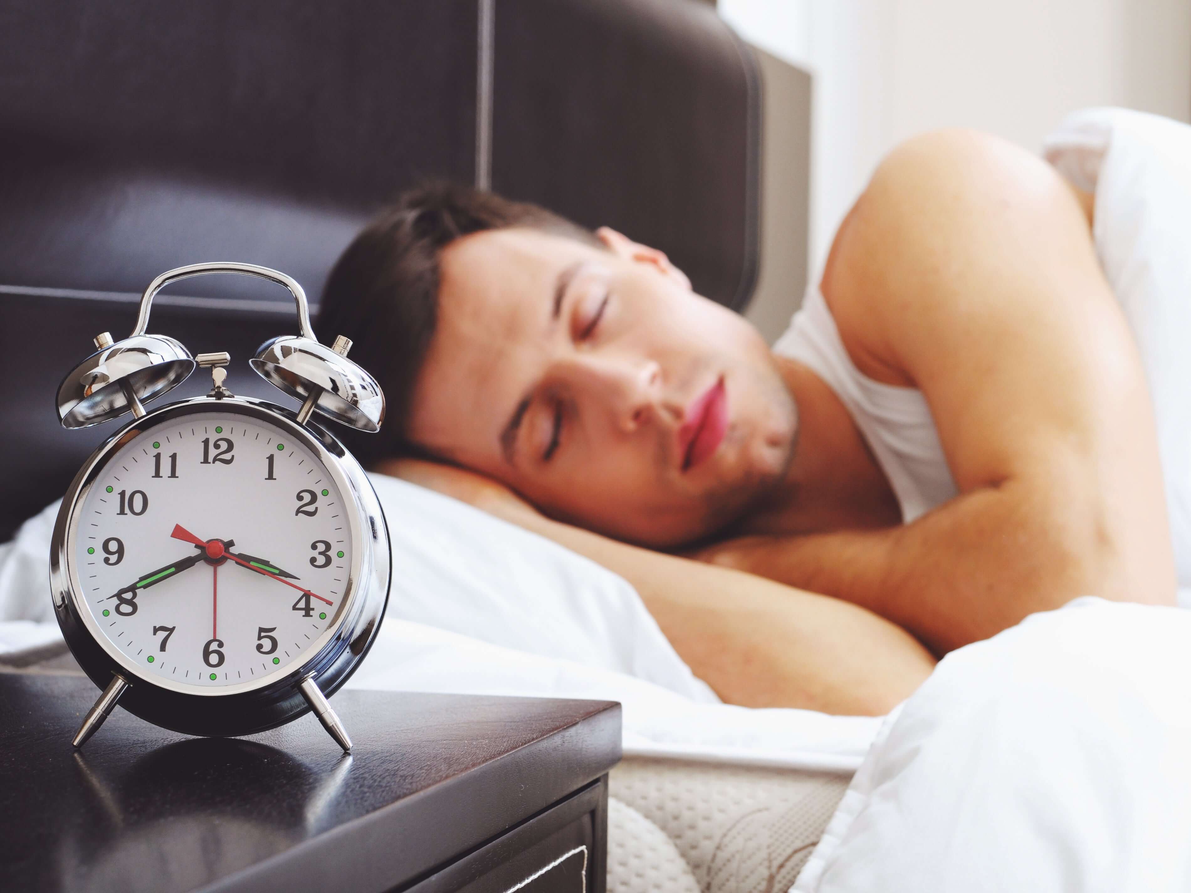 A man sleeping soundly next to an alarm clock, highlighting the importance of sleep quality for health.
