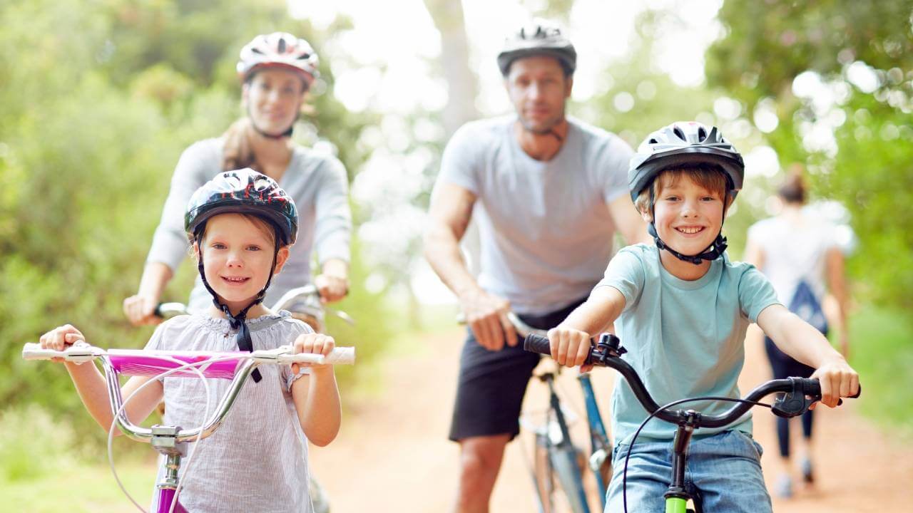 Family cycling together in the park, staying active and pursuing wellness goals this summer.