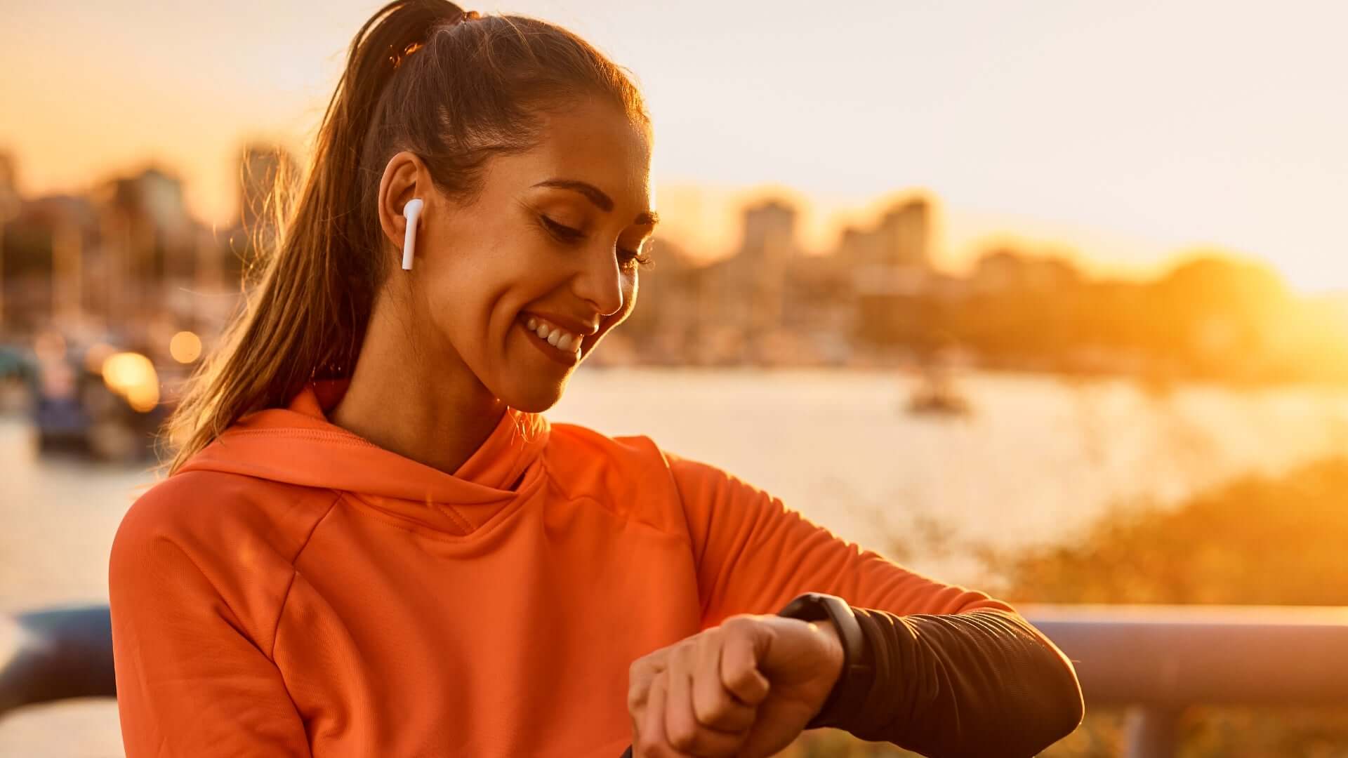 Woman wearing earbuds and looking at a fitness tracker, exploring EMF emitted by earbuds during her workout.