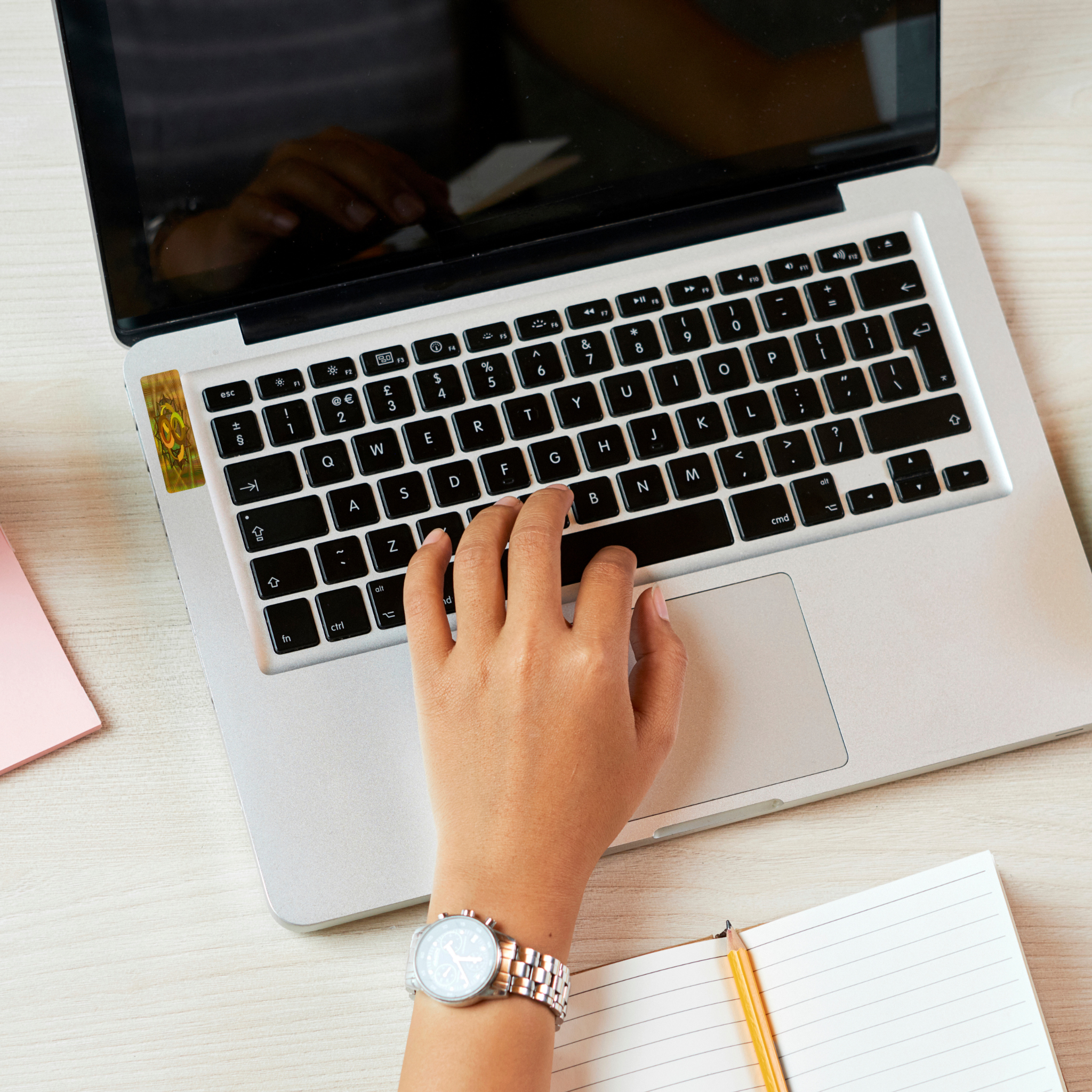 Person typing on a laptop with the Body Align EMF Protect Strips applied, with a notebook and pen on a desk