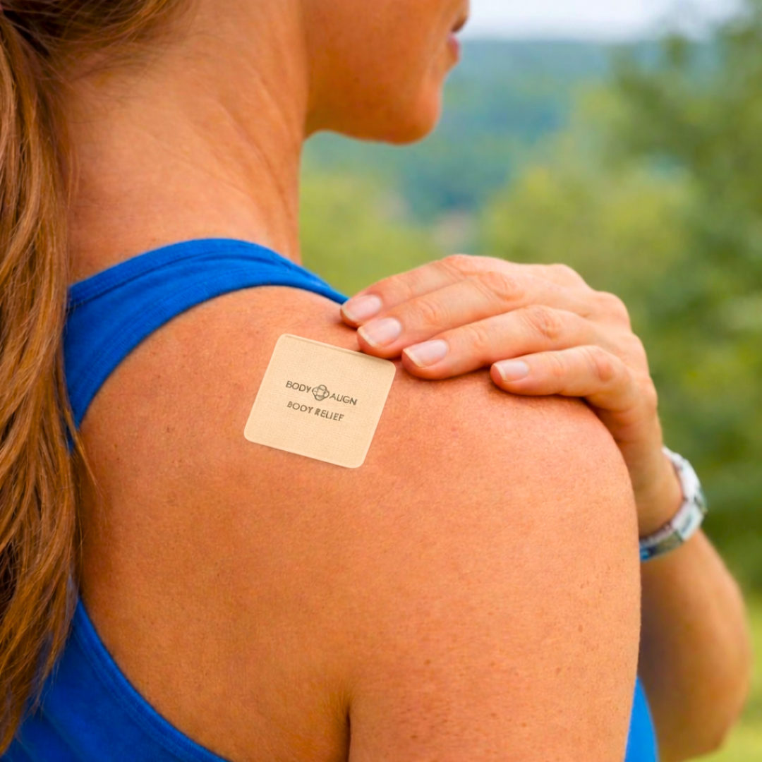 Woman wearing a Body Align Pain Patch on her shoulder with a blurred green outdoor background